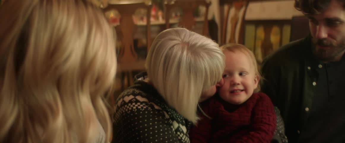 Grandmother hugging and kissin her grandson near his parents at home at christmas