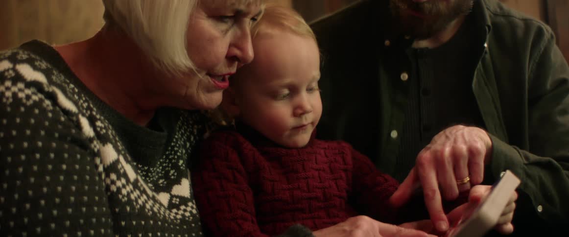 Grandmother reading with her grandson on the couch near his parents at home at christmas