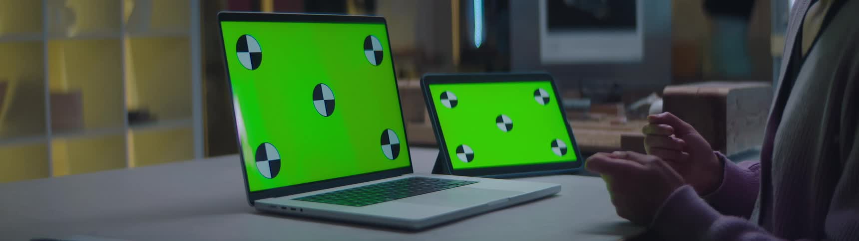 Woman sitting at a desk talking in front of a laptop and a tablet with green replaceable screens