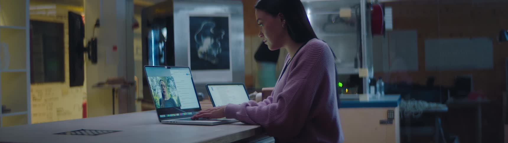 A woman is sitting at a desk in an office at work having a video chat with someone on her laptop in the evening