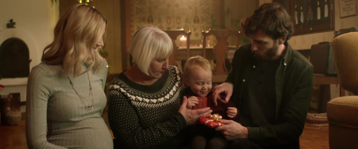 A young boy holding a gift sits on his grandmothers knee next to his mom and dad