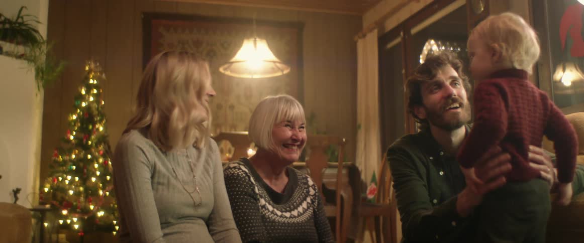 A family is sitting and playing with a toddler in a home during the christmas holidays at night