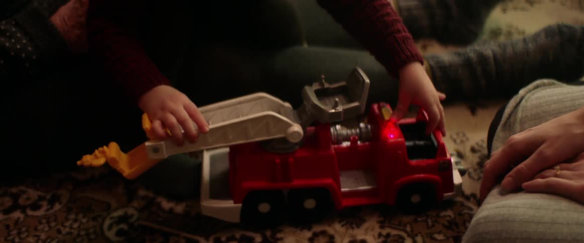 A young boy sits at home on his grandmas knee with his mom and dad and plays with a firetruck