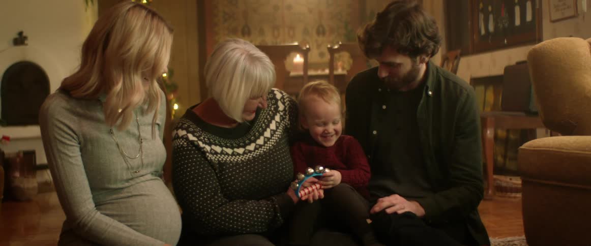 A little boy shakes jingle bells laughing while surrounded by mom dad and grandma
