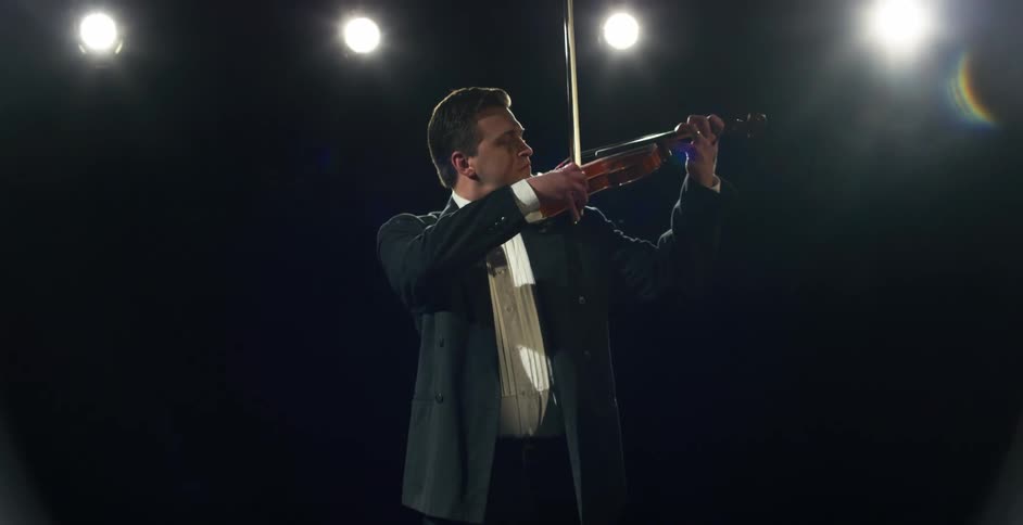 A male violinist in a tux performing on a stage