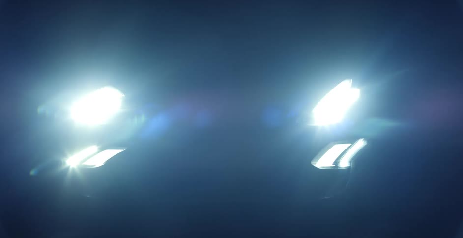 Closeup view of a car with its headlights on is displayed at night