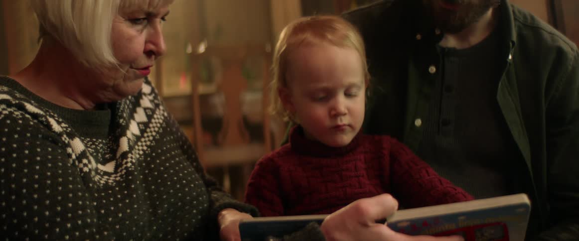 A grandmother reading to her young grandson indoors
