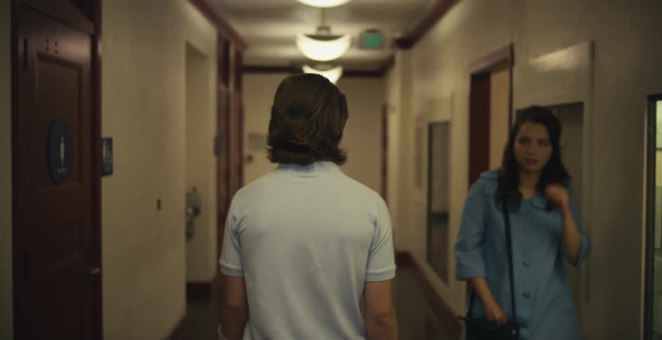 A man wearing an arm cast is walking down a hallway and a woman walks past him and smiles