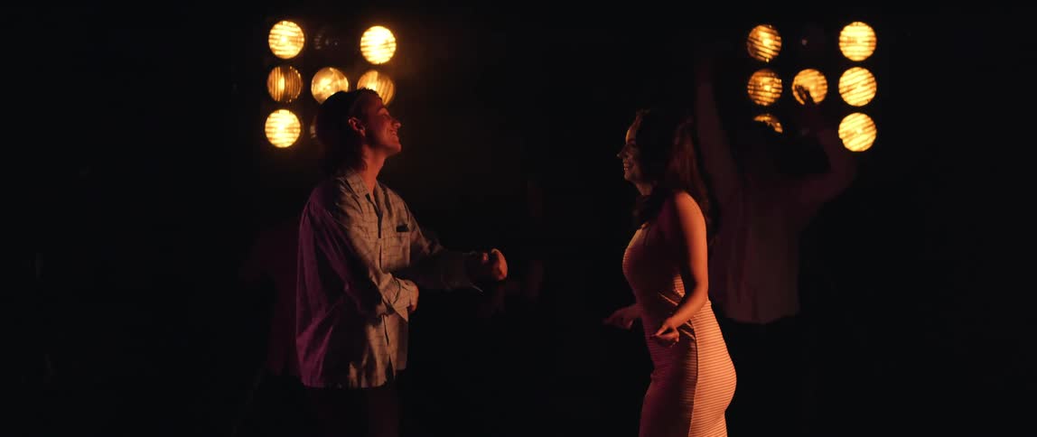 A man and a woman are dancing at a party with other people dancing in the background
