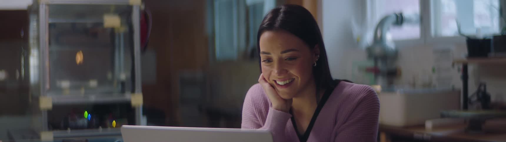 A woman is sitting indoors and typing on a laptop