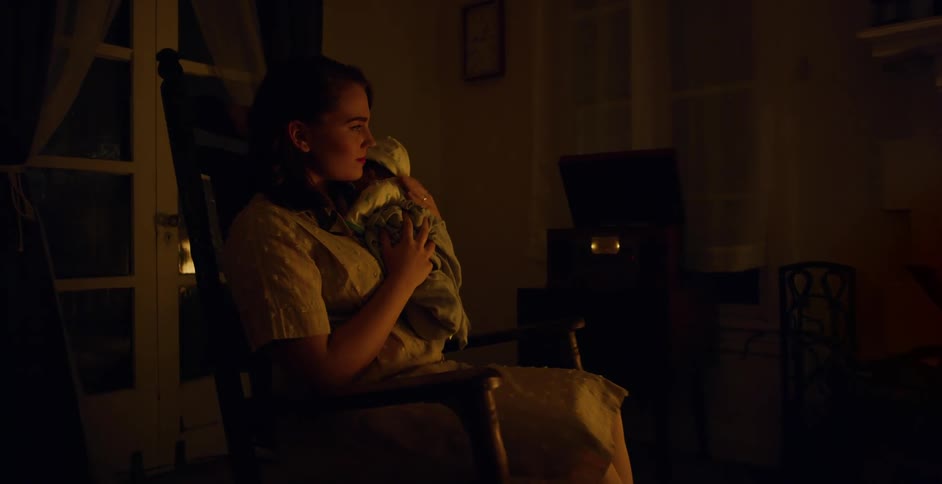 A mother cradles her baby by the fireplace amidst a storm