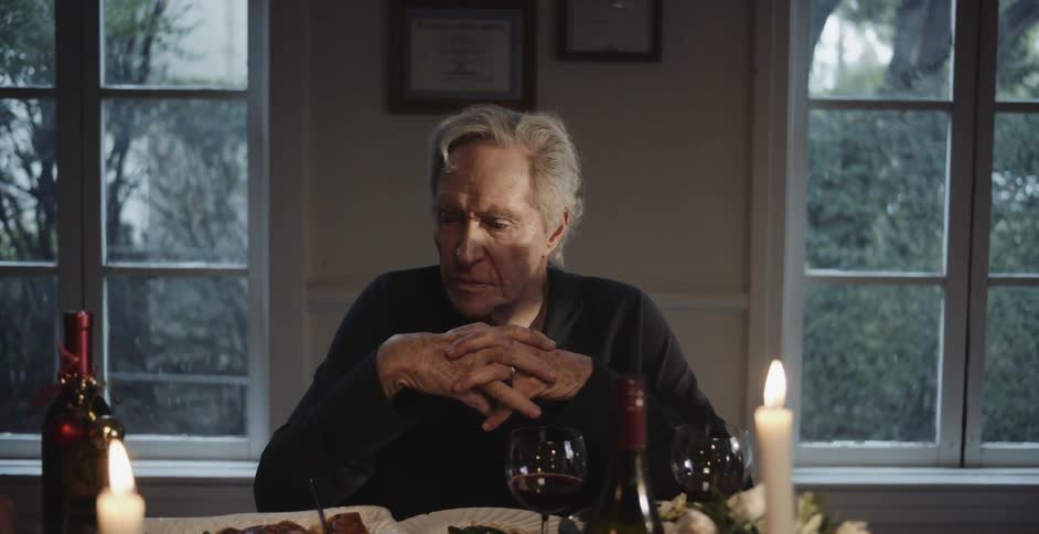 A man sits with his hands intertwined as people chat around him at thanksgiving dinner