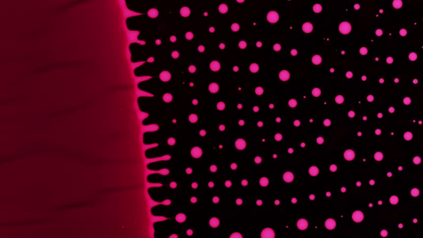 The edges of a red circle drip pink drops outwards into the blackness