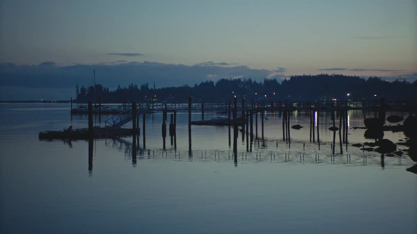 A wooden pier is reflected in the calm water below at dusk