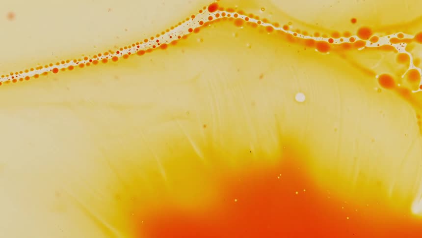 Orange and yellow dye float and swirl in liquid creating bubbles
