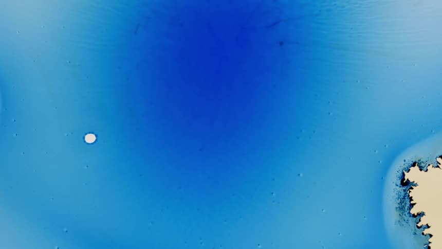 The blue liquid expands and transforms into a pattern of drops