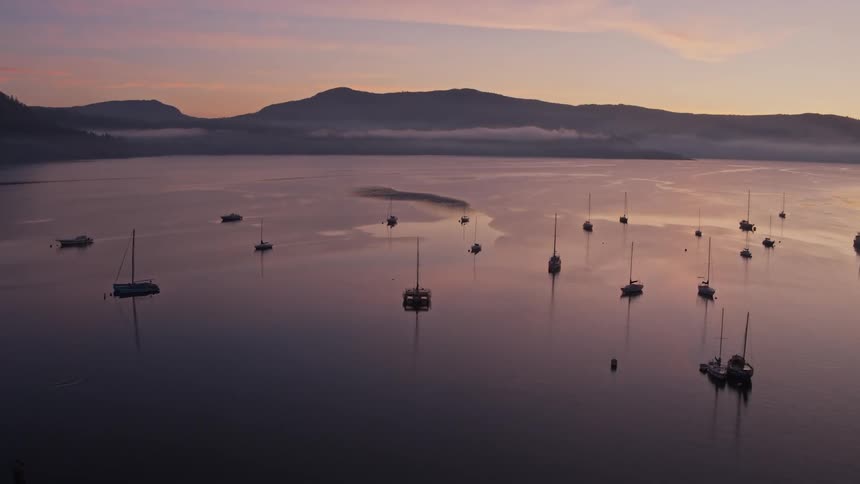 Many boats are anchored in the water at sunrise