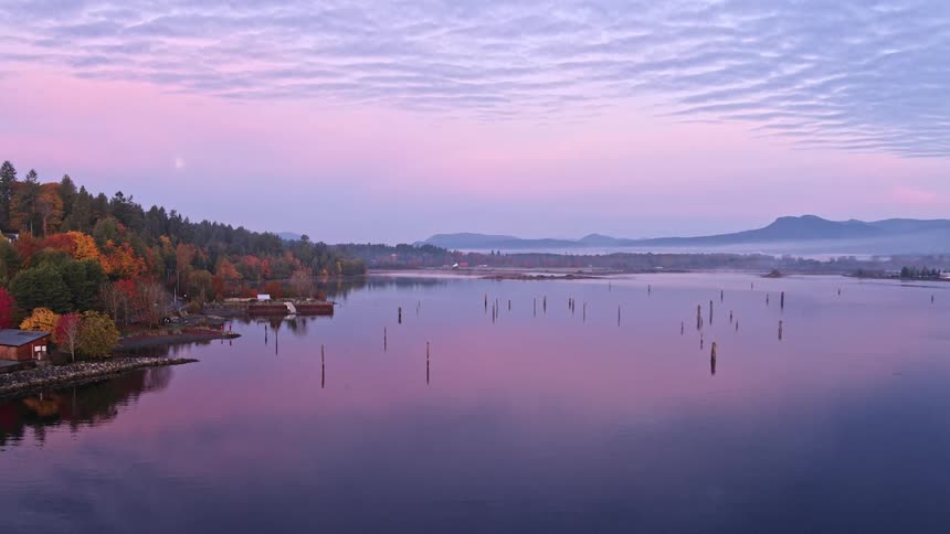 Old dock piles are reflected in a foggy ocean harbor at dusk