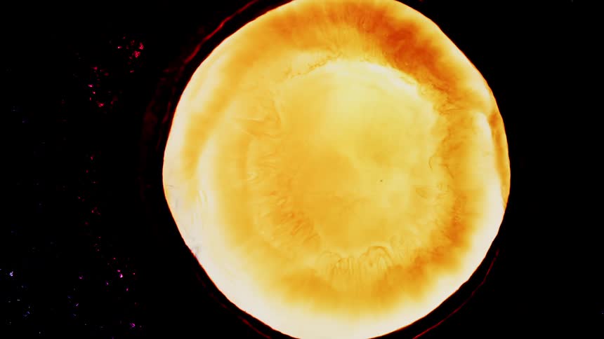 A red orange and yellow circle of colors burst out of a black background like a flaming sun and white emerges from the inside
