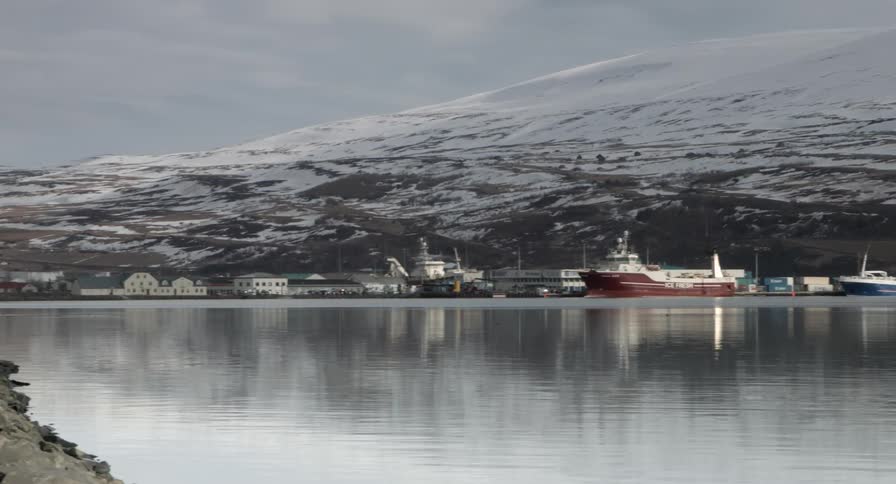 A row of boats are docked near a snow covered hill