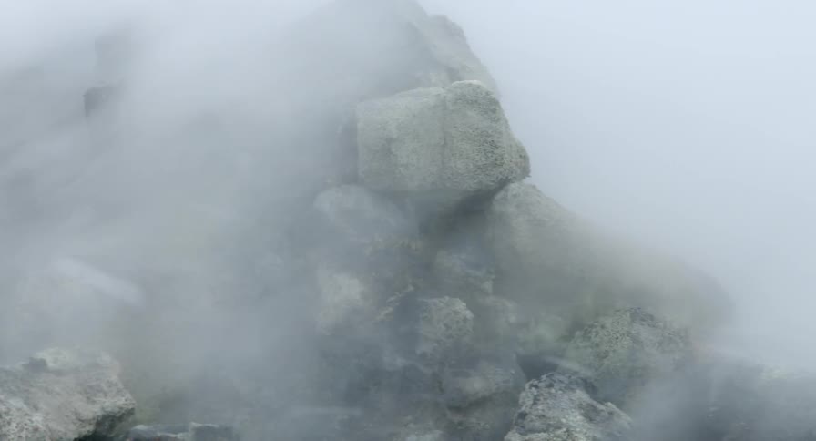 Close up of steam coming from the ground moving across a large pile of rocks