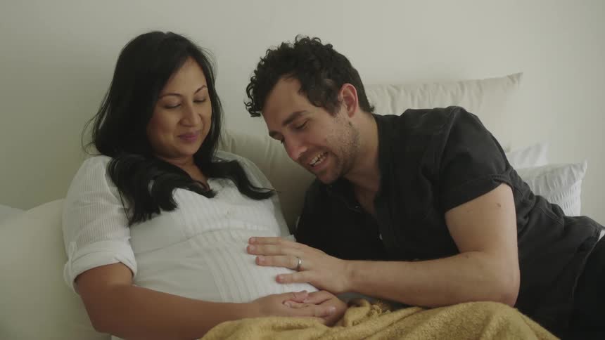 A man listens to his pregnants wife belly and kisses her lips