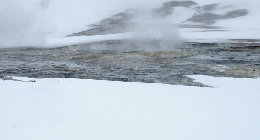 Snow falls on a stream and mists rise above the water