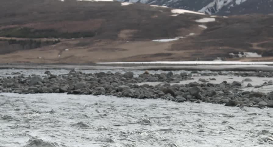 Water flowing on a rocky river with snowy mountains in the background
