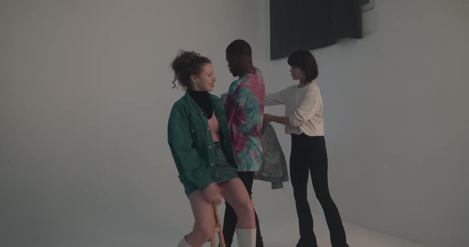 A man and woman are preparing for a photoshoot in a studio with a woman helping with their clothing