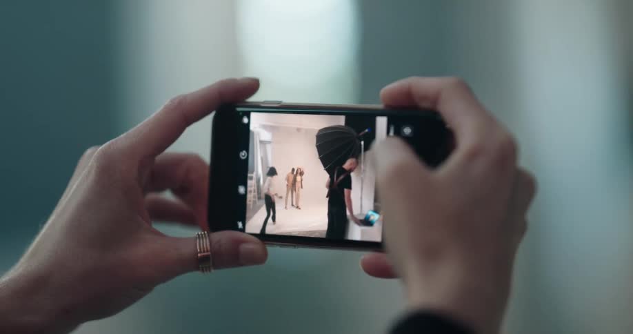 Woman takes pictures with her phone of models posing on a photo shoot