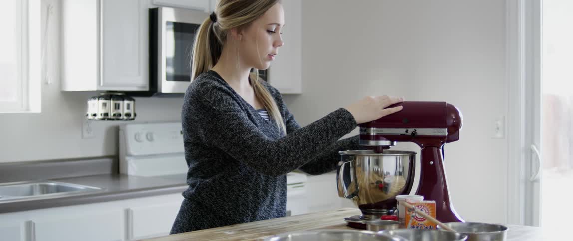 A woman starts a stand mixer sitting on the counter