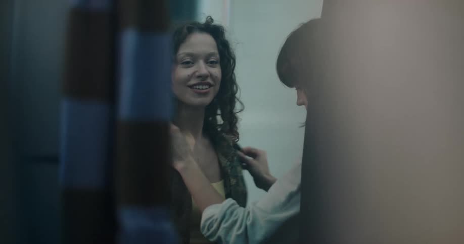 A woman helps another woman put a shirt on over her tank top
