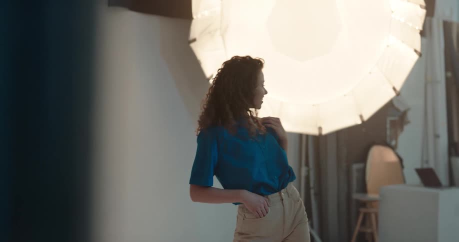 A woman flips her hair back looking over her shoulder and smiling as she poses for a fashion shoot