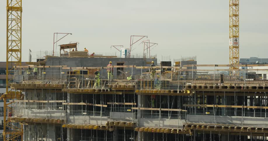 Workers move over upper floor of construction site under a clear sky
