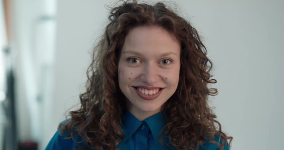Young happy redhead woman standing in a room turns to the camera and smiles