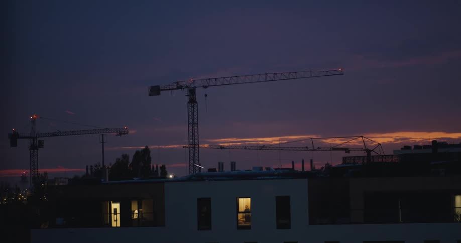 Construction cranes behind a building with a person inside