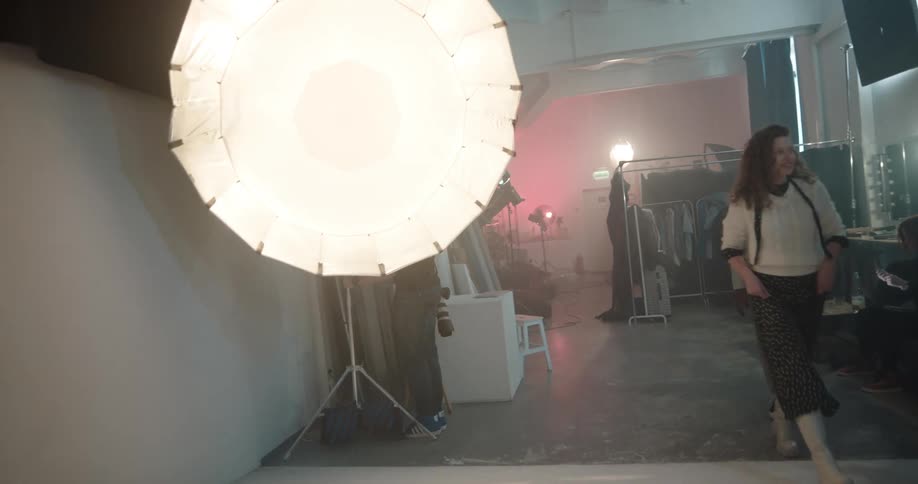 A photographer adjusts equipment at a photo shoot as teenage models walk to get in position for photos