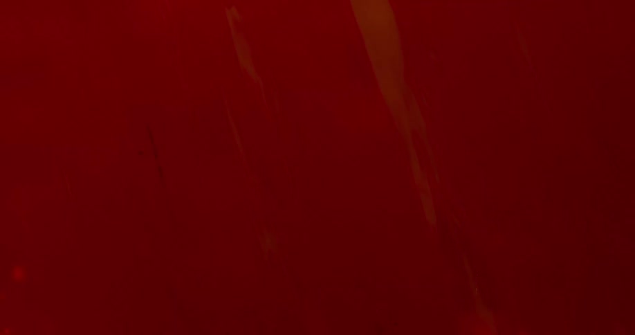 Thick blobs of liquid red ink flowing down a backlit translucent surface