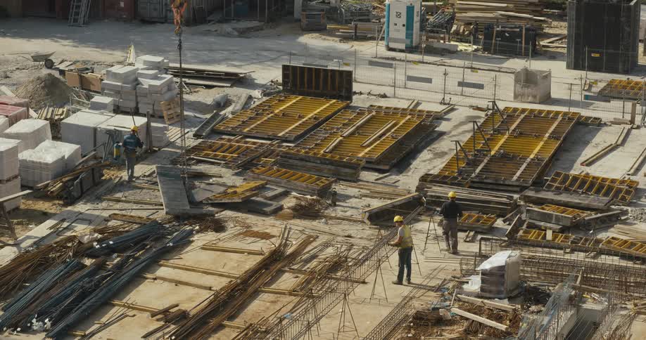 A construction crew is working on a site and a crane lifts a piece of the building