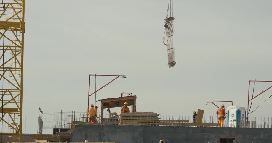 A construction crew is working on a building as a crane is lowering a large piece into the construction site