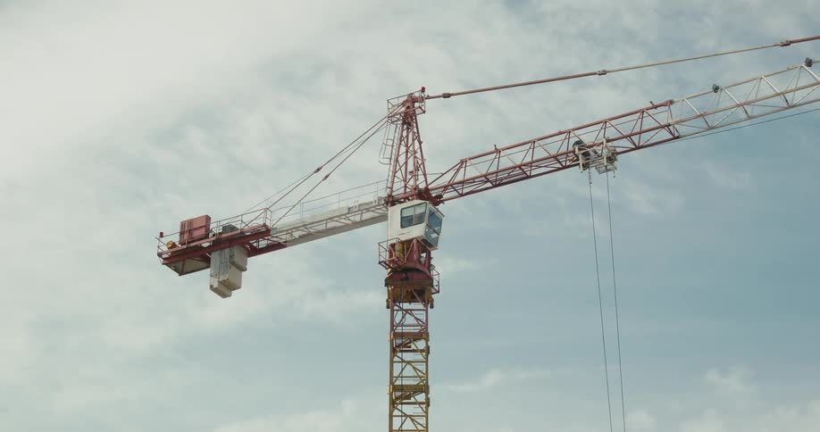 Big orange construction crane moving from right to left in front of the blue sky