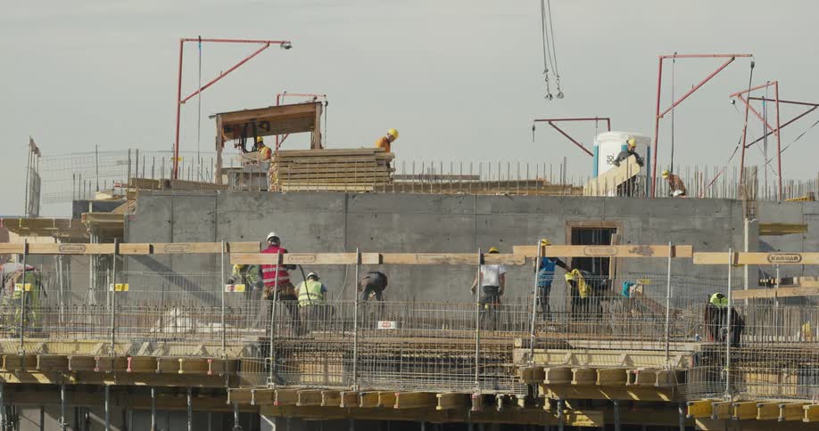 A construction crew is on a building working and cranes are lifting supplies
