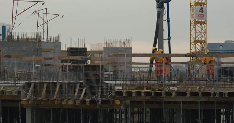 Group of workers wearing hardhats and protective equipment pouring concrete at a construction site