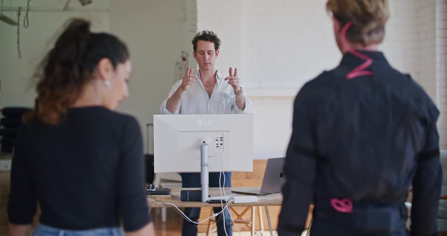 Man in white shirt gives instructions to another man wearing a futuristic motion capture black suit