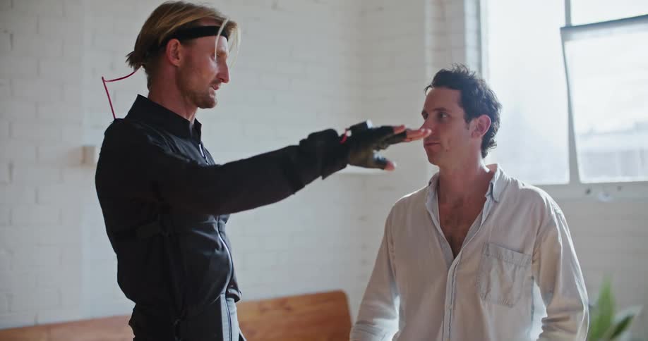 Man in white shirt gives instructions to another man wearing a futuristic black suit