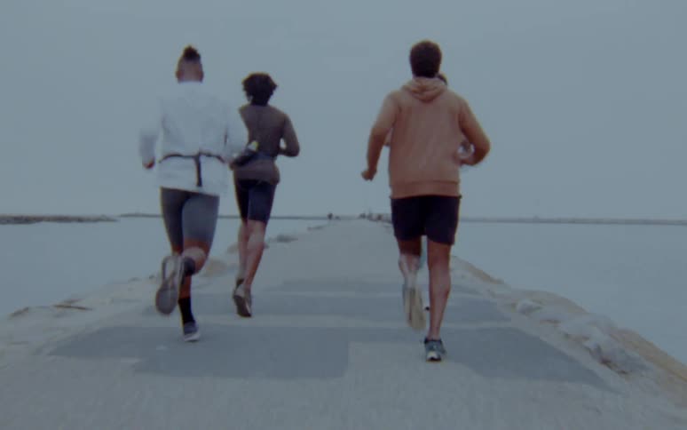 Four men are jogging outdoors by a body of water