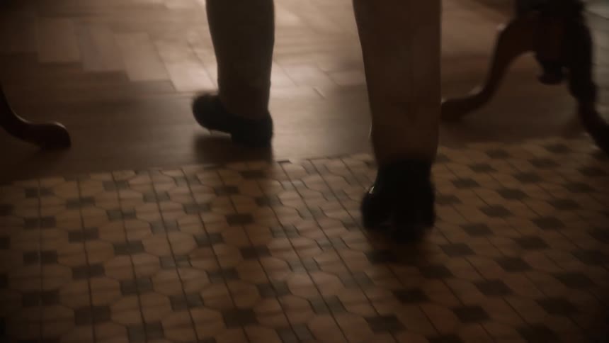 A man walks along a tile and wood floor