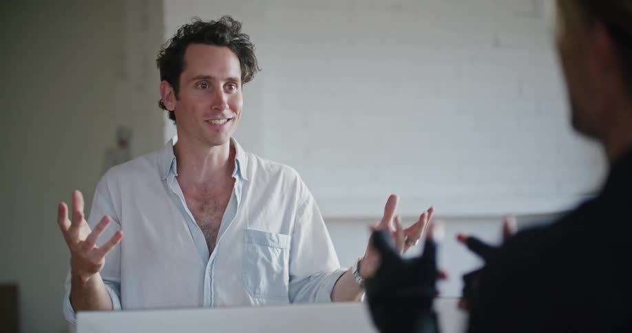 Man in white shirt gives instructions to another man wearing a futuristic motion capture black suit