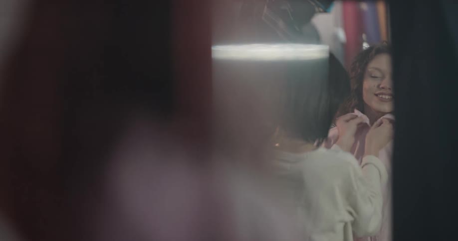 Female assistant helps woman try on pink shirt in clothing store