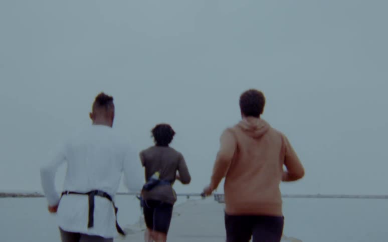 A group of four men jogging on a pier on a gray cold day